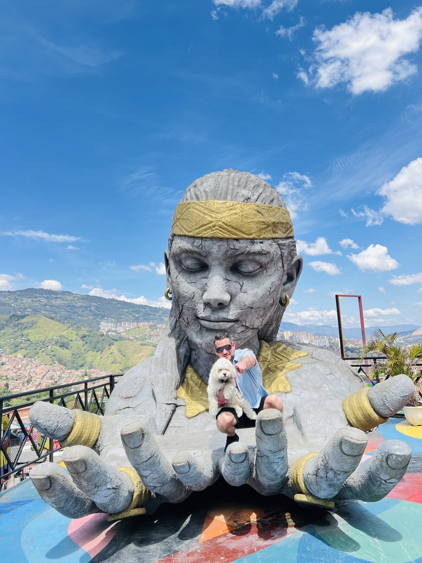 Adam and Maya sitting in the hands of a giant statue above the city