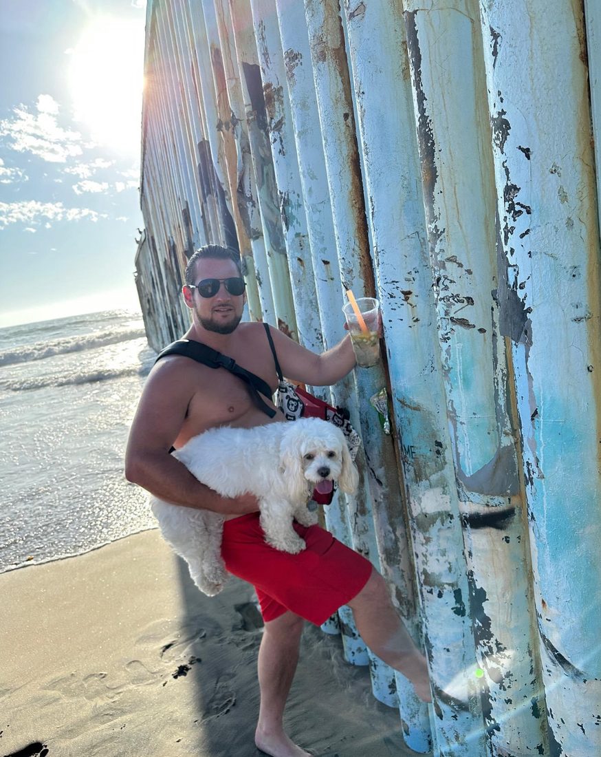 Adam holding Maya beside the border wall on the beach